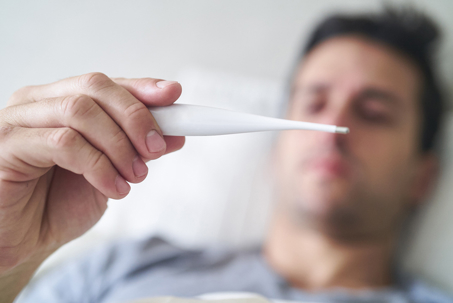 man holding a thermometer while in bed